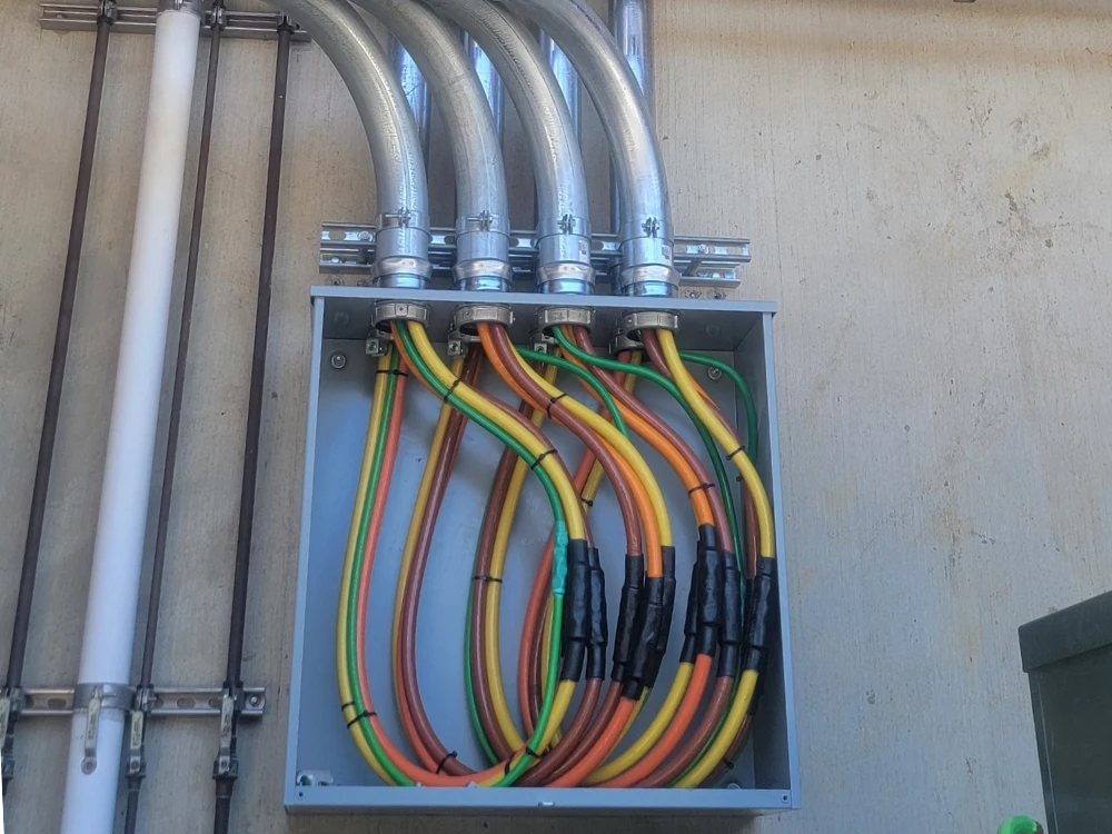 Open commercial electrical junction box showing neatly routed thick color-coded wiring and overhead metallic conduit runs installed along a concrete wall.